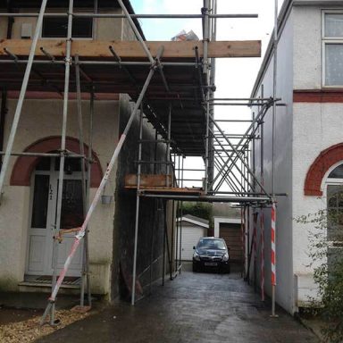 Scaffolding between two buildings with a car parked beside them.