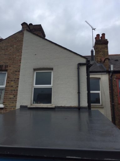 View of the side of a house with a cloudy sky and part of a sloped roof.