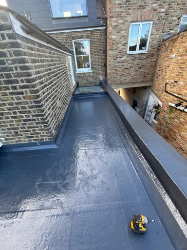 Flat roof with a grey surface and nearby brick walls, with windows visible in the background.