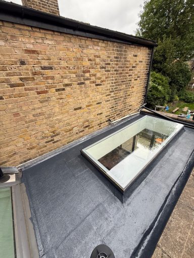 Flat roof with a skylight and a brick wall in the background.