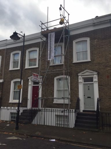Scaffolding outside a brick townhouse with two doors and a street lamp nearby.